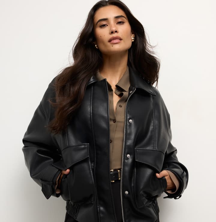 Model is wearing a black faux leather jacket over a brown top and black pants.