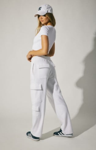Model is wearing white fleece bottoms, a white crop top, and a logo hat.
