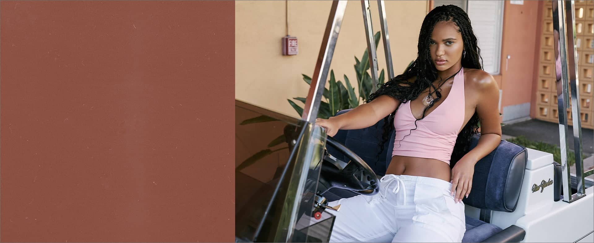 Model sits on top of a block wearing a pink tube top, a white shrug, and denim bermuda shorts with white sneakers.