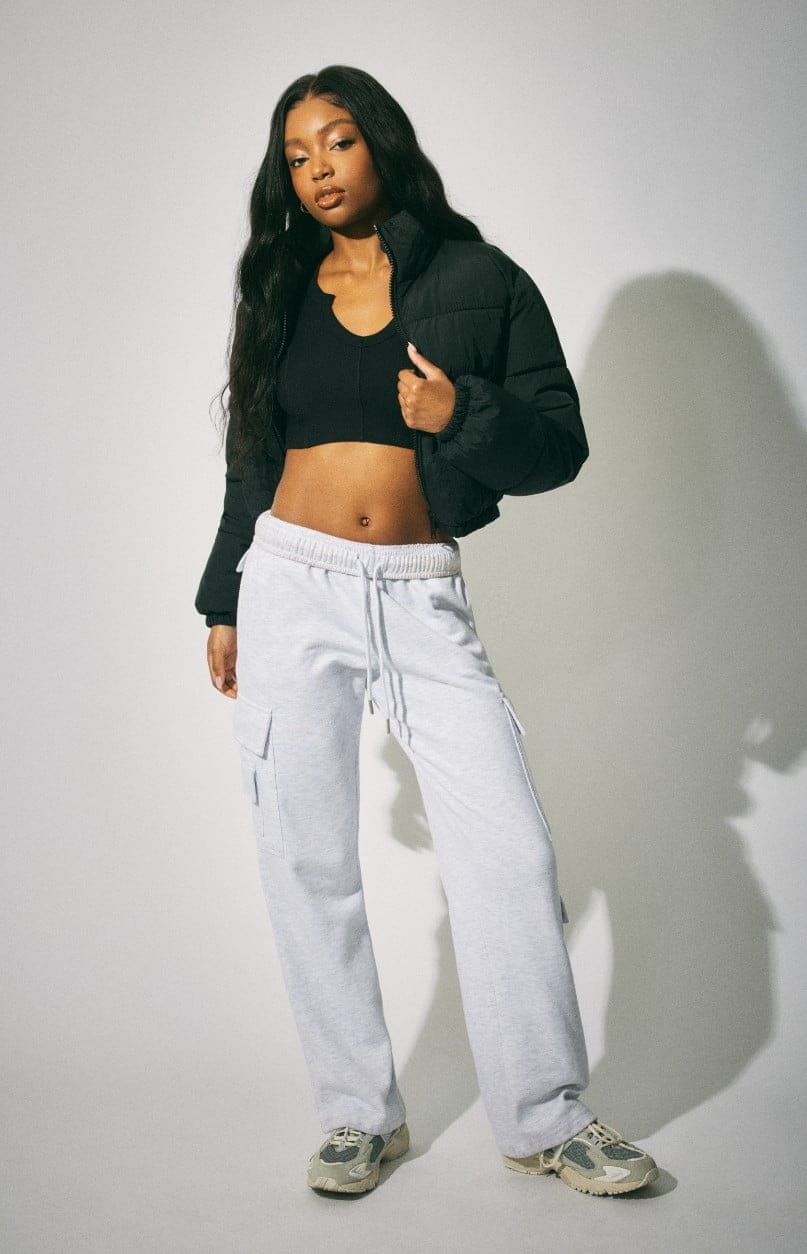 Model wears a black puffer with a cropped black top and grey sweats.