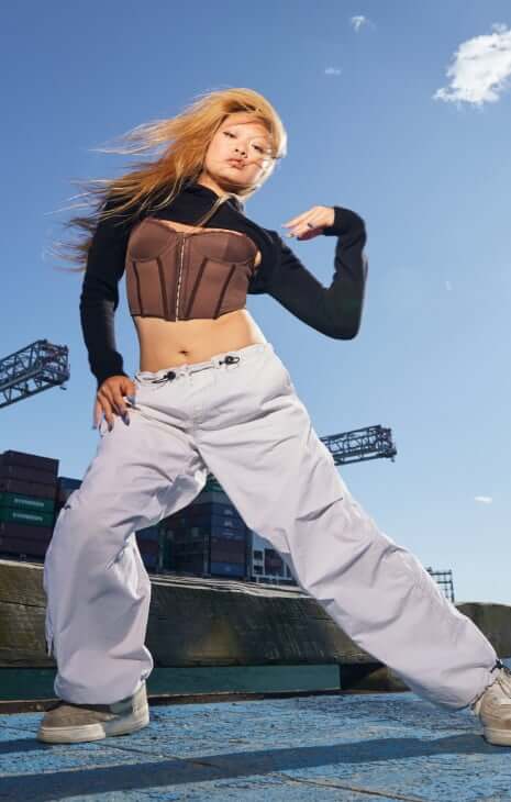 Model is wearing a corset, black shrug, and parachute pants.