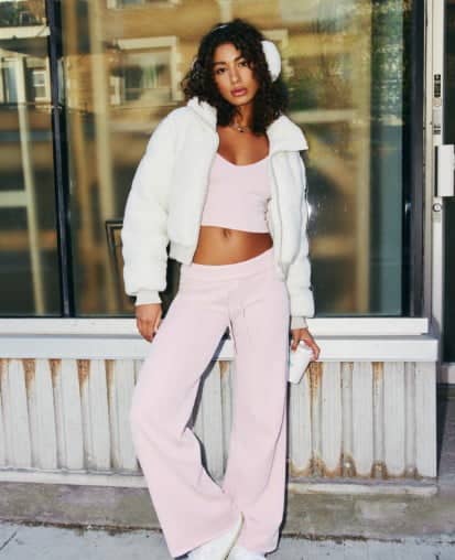 Model poses in a white puffer and a pink tank top and matching sweats.