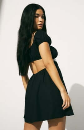 Model is wearing a black mini dress with puff sleeves and cut-out detailing.
