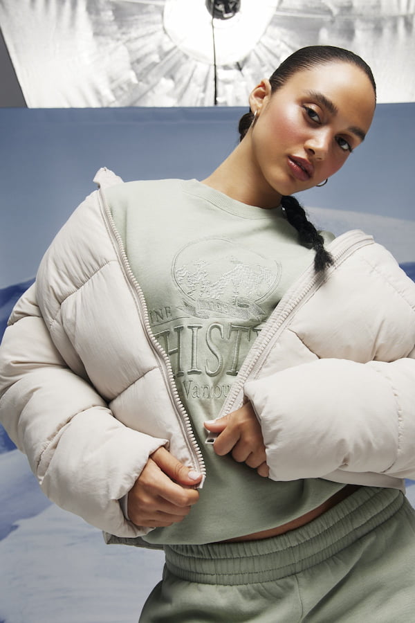 Model is wearing a light green sweatsuit and a white puffer.