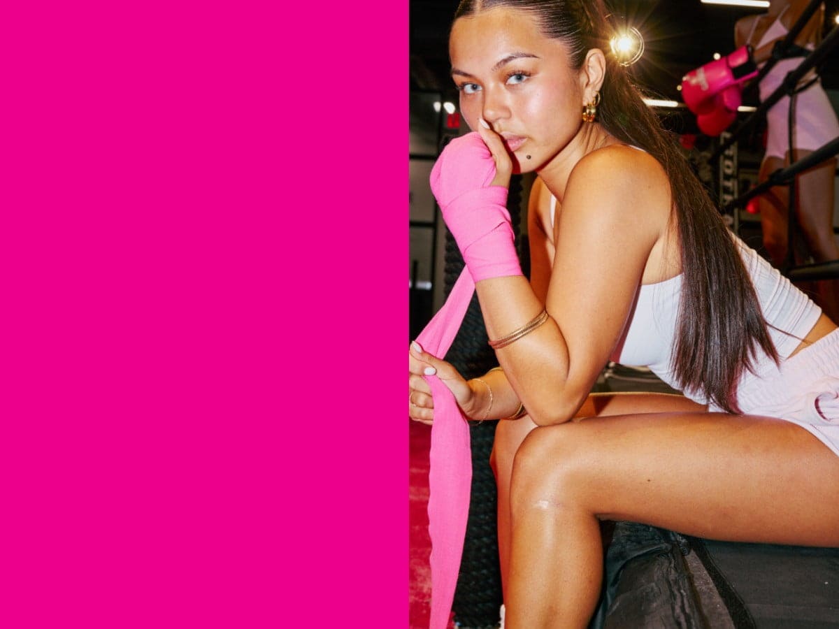 Model posed while seated wearing a white tank top, punch pink shorts, and bright pink tape-wrapped hands.