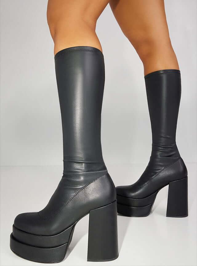 Model is wearing knee high boots with chunky heel.